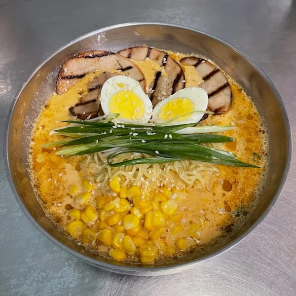 Ramen bowl with noodles, corn, green onions, sliced pork, and two halved boiled eggs.