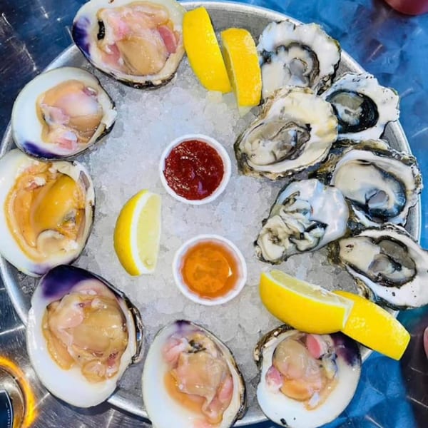 A platter of fresh Big T's oysters and clams on ice with lemon wedges and sauces.