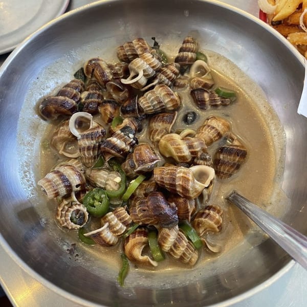 A metal bowl filled with cooked sea snails in a creamy sauce with green peppers.